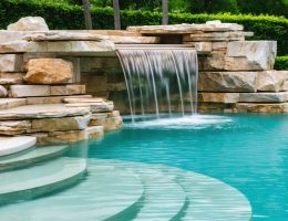 Serene luxury natural stone pool surrounded by elegant landscaping with cascading waterfalls and varying stone textures.