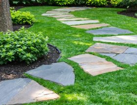 A beautifully crafted stone pathway in a backyard, made from a mix of locally sourced flagstone, slate, and limestone, surrounded by lush greenery, embodying sustainability and natural aesthetic integration.