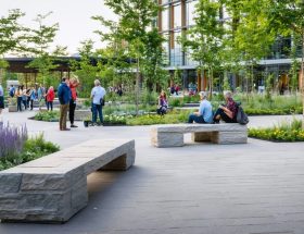 People of diverse backgrounds enjoying the natural stone benches in a beautifully landscaped urban park, surrounded by lush native plants and modern architectural features.