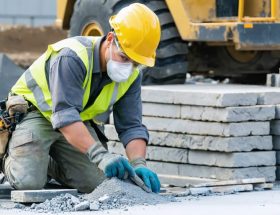 A stone installation worker wearing complete personal protective equipment, including a hard hat, safety glasses, dust mask, gloves, and steel-toed boots, showcasing the importance of PPE in a work setting.