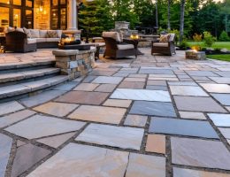 A stunning natural stone patio with various stone materials like flagstone, slate, and limestone arranged in a harmonious pattern at sunset, surrounded by greenery and stylish patio furniture.