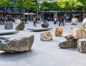 Urban plaza with modern natural stone sculptures, featuring people interacting with and admiring the varied textures and colors of the installations, accentuated by dynamic play of light and shadow.