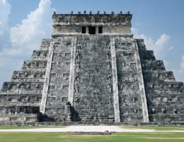 Image of an ancient Aztec temple featuring towering stone sculptures, intricately carved reliefs, and free-standing figures, showcasing the blend of artistry and architectural design, set against a Mesoamerican cityscape.