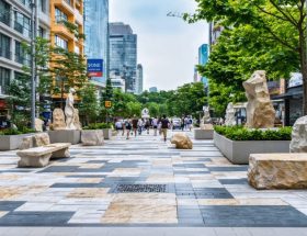 An urban street scene featuring diverse natural stone installations, including mosaics and sculptures, blending traditional craftsmanship with modern design in a sustainably crafted public space.