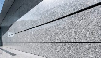 "An elegant granite wall cladding on a modern building facade with a blurred urban skyline in the background."