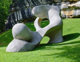 A stone sculpture artistically blended into a hillside, with surrounding natural rock and greenery creating a harmonious setting that emphasizes the connection between the sculpture and its environment.