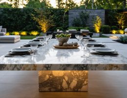 Outdoor setting with a luxurious natural stone table, showcasing marble veining and contemporary dining setup amidst a lush garden environment.