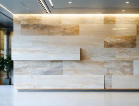 Modular natural stone wall panel being lifted to reveal concealed aluminum rail and mechanical clips in a modern office, illustrating a reconfigurable, sustainable installation system.