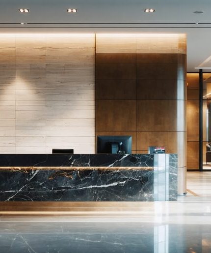 Contemporary commercial lobby with a polished granite reception desk, limestone feature wall, and quartzite flooring lit by soft daylight, with a blurred corridor and glass-walled conference room in the background.
