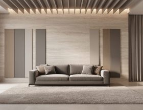 Contemporary living room with a honed limestone feature wall and stone floor, complemented by neutral fabric acoustic panels, suspended ceiling baffles, a thick area rug, upholstered seating, and lined drapery under soft natural daylight.