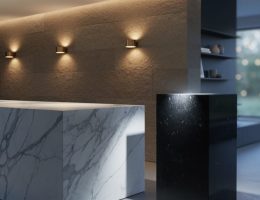 Modern interior vignette with a veined white marble island lit by cool daylight, a limestone wall glowing under warm sconces, and a polished black granite pedestal reflecting an accent spotlight; layered lighting creates depth and highlights stone textures.