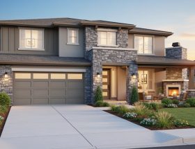 Two-story contemporary home with ledgestone accent wall framing the entry and garage, photographed at golden hour with landscaped front yard and a covered patio with stone fireplace in the background.