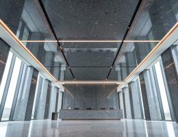 Low-angle view of a modern lobby showcasing a polished granite ceiling with coffered panels, reveal joints, and recessed LED lighting, with a minimal reception desk and stone walls fading into the background.