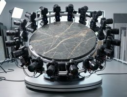 Circular array of DSLR cameras forming a photogrammetry rig around a veined natural stone slab on a motorized turntable in a studio, side-lit to highlight texture, with workshop equipment softly blurred in the background.