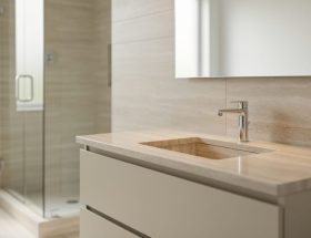 Modern bathroom with a light honed stone vanity countertop, minimalist faucet, and frameless shower in a bright spa-like setting.