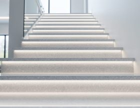 Low-angle view of a modern indoor staircase with glossy quartz treads and risers and subtle LED underlighting glow.