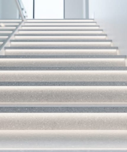Low-angle view of a modern indoor staircase with glossy quartz treads and risers and subtle LED underlighting glow.