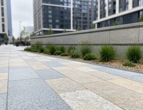 Eye-level view of a modern urban plaza with natural stone pavers, a low retaining wall, and integrated greenery.