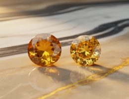 Close-up of polished yellow gemstones, including citrine and yellow sapphire, resting on a warm marble-like stone surface with golden reflections.